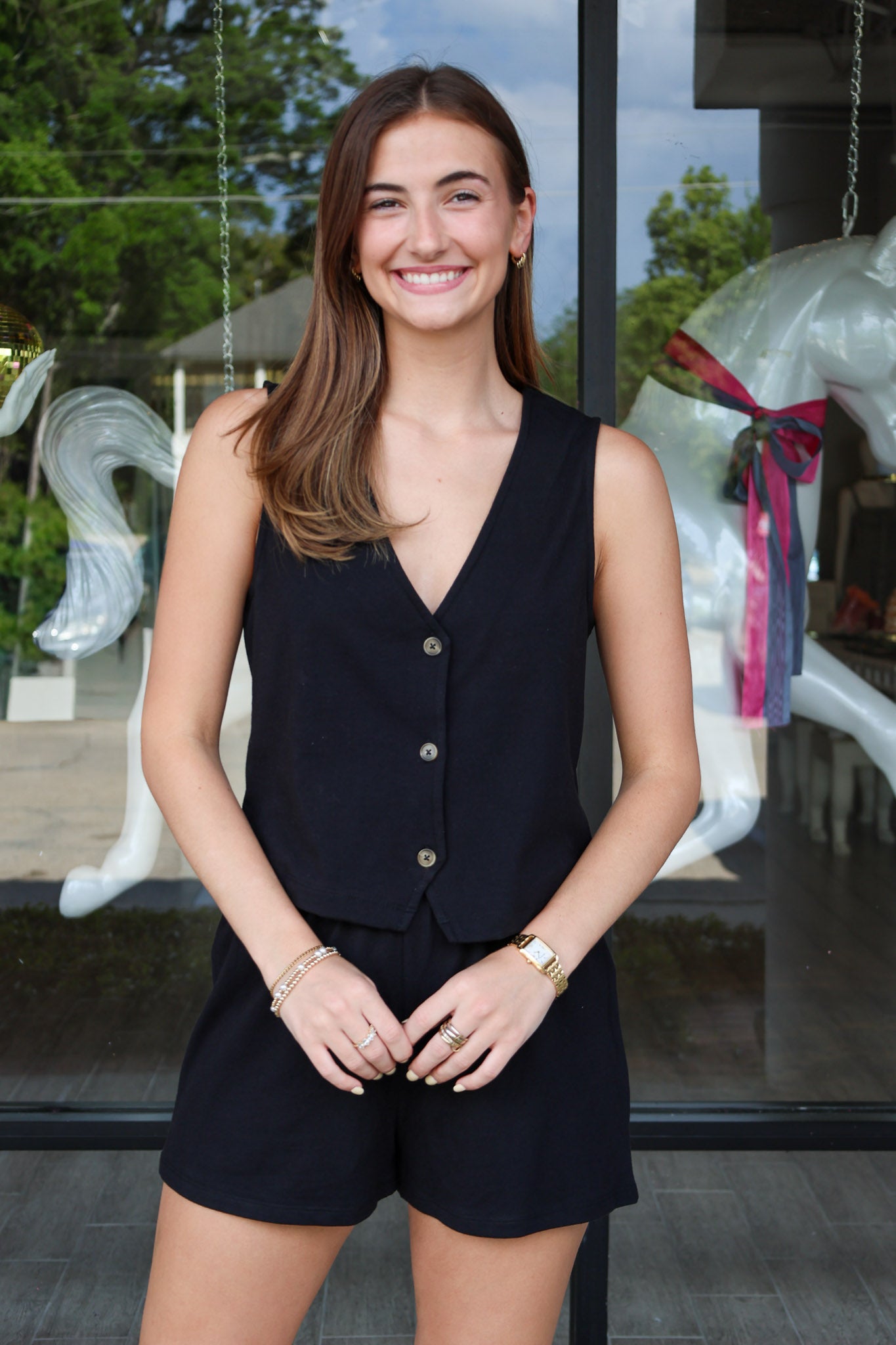 Woman wearing a black sleeveless top and shorts standing in front of a glass door with decorative elements.