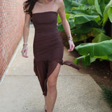 Woman in a brown dress walking on a sidewalk with greenery in the background