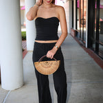 Woman in black outfit holding a wooden handbag on a sidewalk.