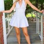 Woman in a white striped dress standing on a wooden deck with greenery in the background
