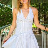 Woman wearing a light blue striped halter mini dress on a wooden deck with greenery in the background
