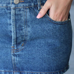 Person wearing a blue denim skirt with a plain background