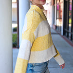 Woman wearing a yellow and white striped sweater and denim shorts standing on a sidewalk.