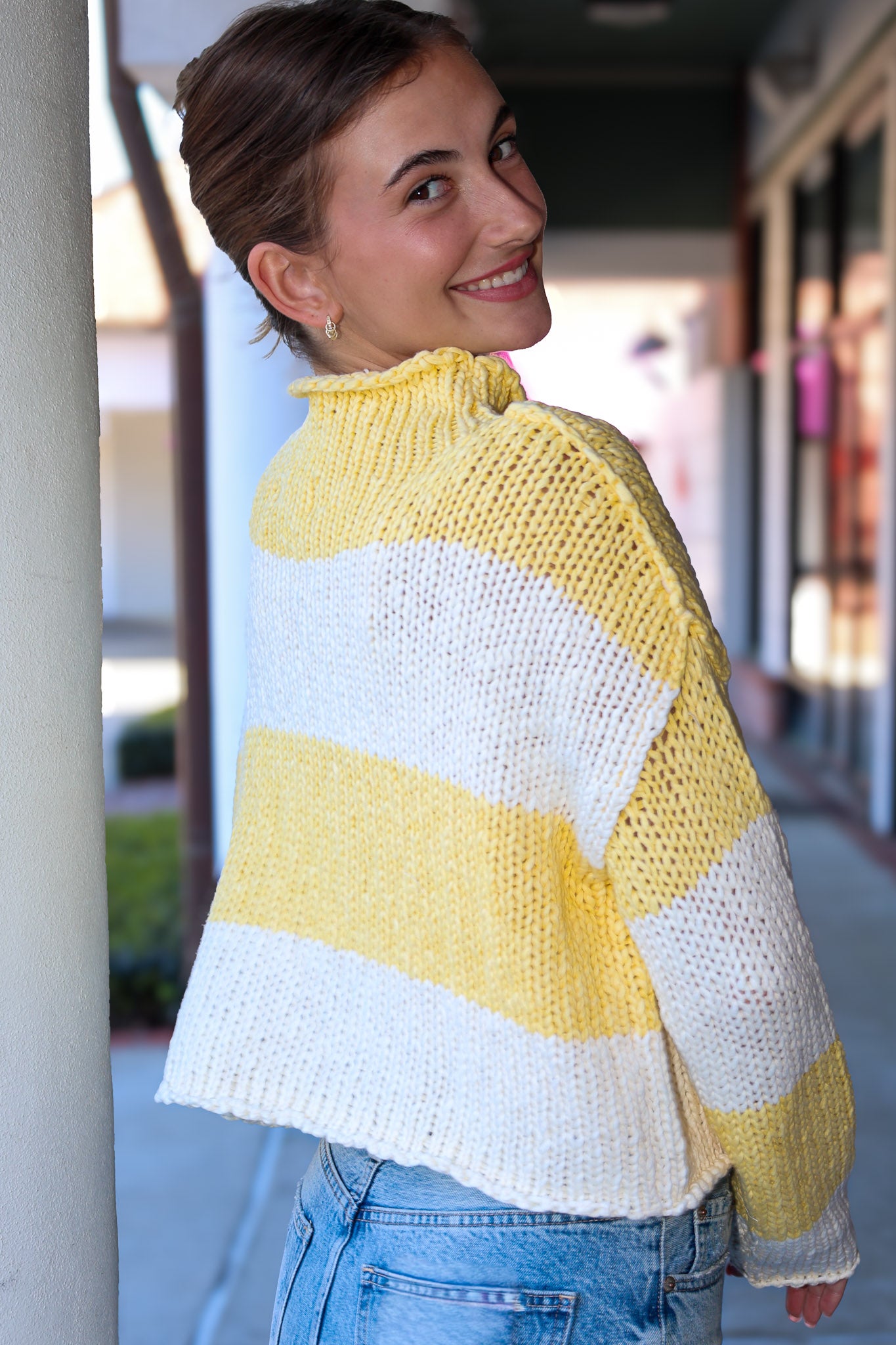 Woman wearing a yellow and white striped sweater standing outdoors.