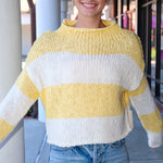 Person wearing a yellow and white striped sweater with denim shorts, standing outdoors.