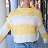 Person wearing a yellow and white striped sweater with denim shorts, standing outdoors.