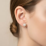 A pair of stud earrings with white pearls and gold-toned halo settings, displayed on a pink Rodéo Boutique card against a light gray background.