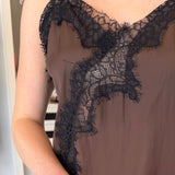 A close-up of a person wearing a sheer taupe-brown camisole with black lace trim along the neckline and armholes.