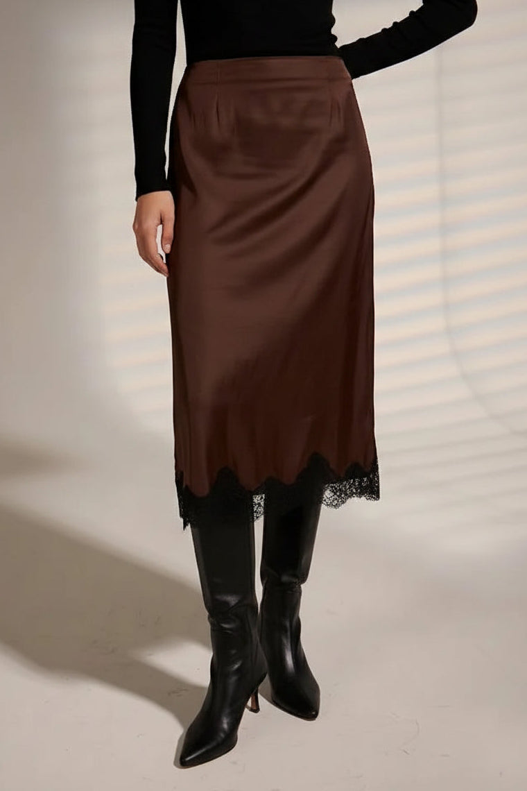 A model wearing a brown satin midi skirt with a black lace hem, styled with a black long-sleeve top and black pointed-toe ankle boots.