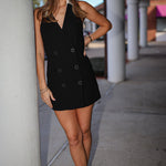 Woman in a black mini blazer dress standing on a sidewalk with columns in the background