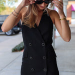 Woman wearing a black sleeveless blazer dress on a city street.