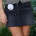 Person wearing a black Pistola denim skirt with a visible brand label, standing outdoors.