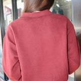A person viewed from behind wearing a dusty rose or muted terracotta long-sleeve cropped sweatshirt with a relaxed collar, paired with blue jeans, standing in front of a glass storefront.