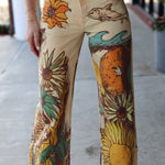 Hand-painted jeans with sunflower and wave designs on a concrete floor.