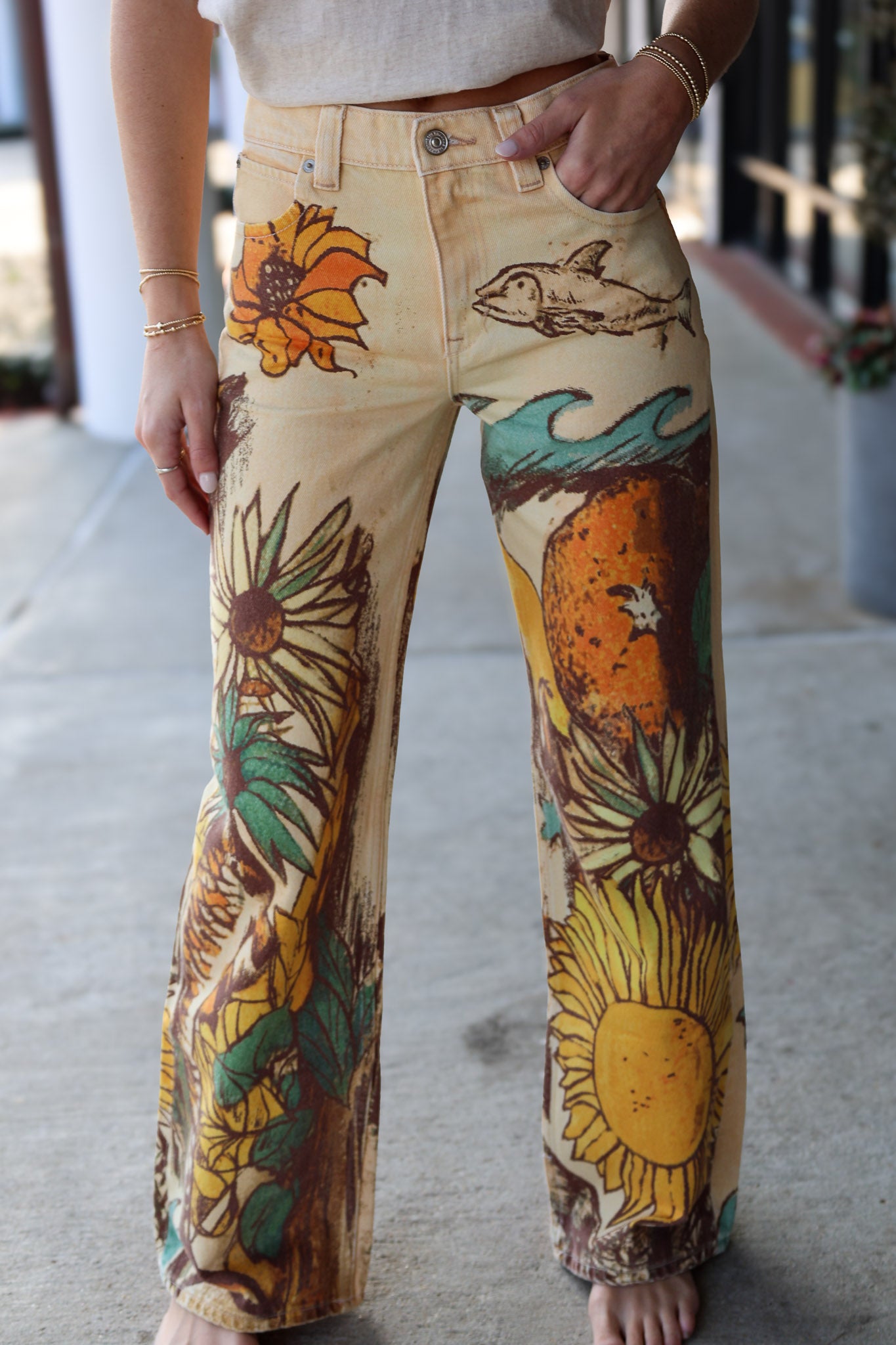 Hand-painted jeans with sunflower and wave designs on a concrete floor.