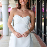 Woman in a white strapless dress standing outdoors on a sidewalk.