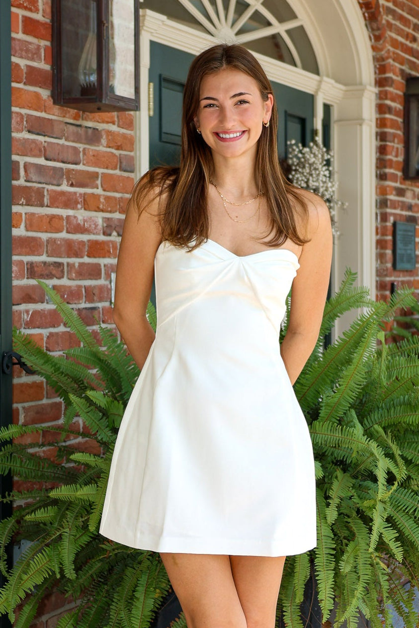 Woman in a white dress standing in front of a brick building with greenery.