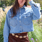 Person wearing a denim jacket and brown skirt in an outdoor setting with grass and flowers.