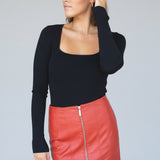 Woman wearing a black long-sleeve top and red leather skirt against a plain background