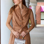 A woman wearing a sleeveless tan faux-suede belted vest and matching shorts, holding a clear vinyl clutch with gold hardware,  at Rodéo Boutique.