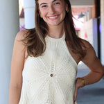 Woman wearing a white sleeveless top with a textured pattern, standing outdoors.