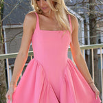 Woman wearing a pink dress standing outdoors with trees and a building in the background.