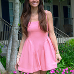 Woman in a pink dress standing outdoors with greenery and flowers in the background