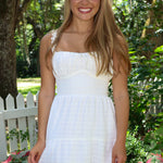 Woman in a white dress standing outdoors with greenery and a white picket fence in the background