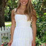 Woman in a white dress standing outdoors with greenery and a white picket fence in the background