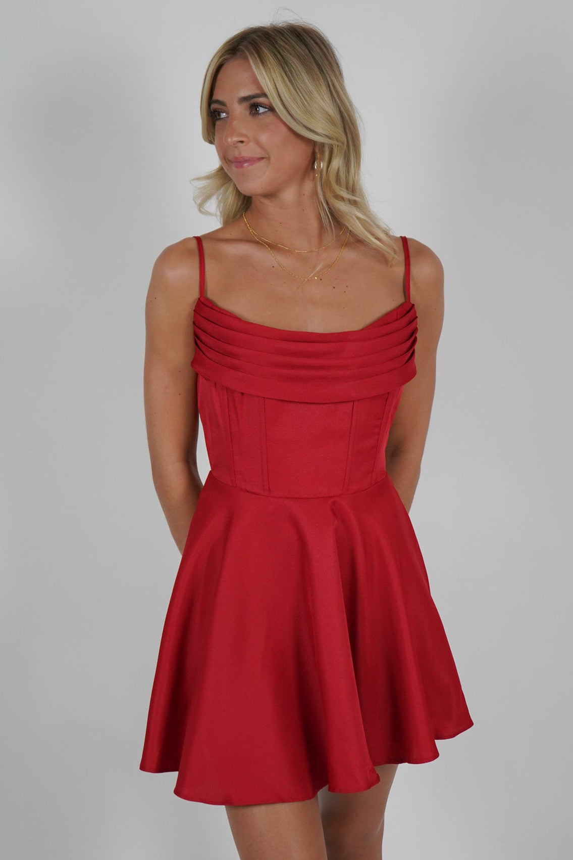 A woman standing, wearing a vibrant red, sleeveless mini dress with a round neckline.