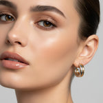 A pair of small hoop earrings with a gold and silver split design, displayed on a pink card labeled 'Rodéo BOUTIQUE'.