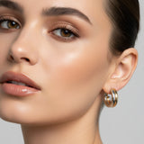 A pair of small hoop earrings with a gold and silver split design, displayed on a pink card labeled 'Rodéo BOUTIQUE'.