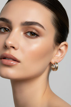 A pair of small hoop earrings with a gold and silver split design, displayed on a pink card labeled 'Rodéo BOUTIQUE'.
