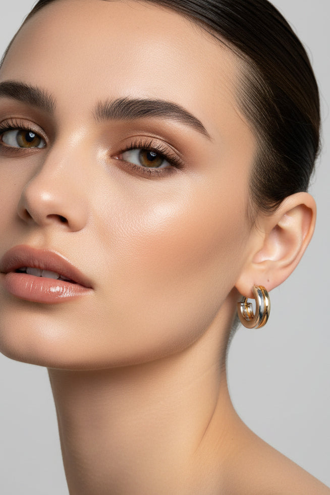 A pair of small hoop earrings with a gold and silver split design, displayed on a pink card labeled 'Rodéo BOUTIQUE'.