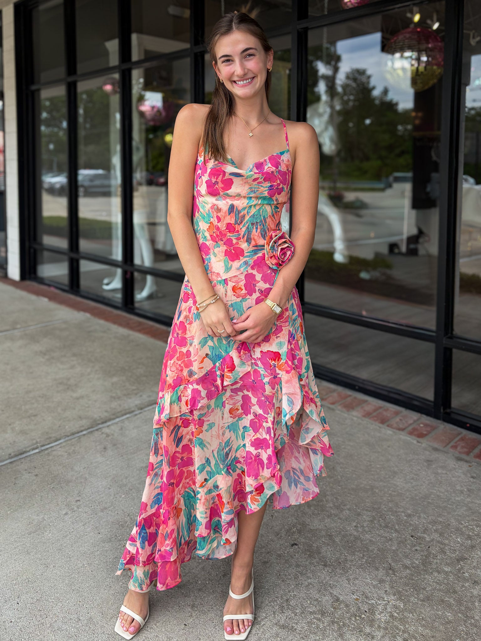 Woman wearing a colorful floral dress standing on a sidewalk.