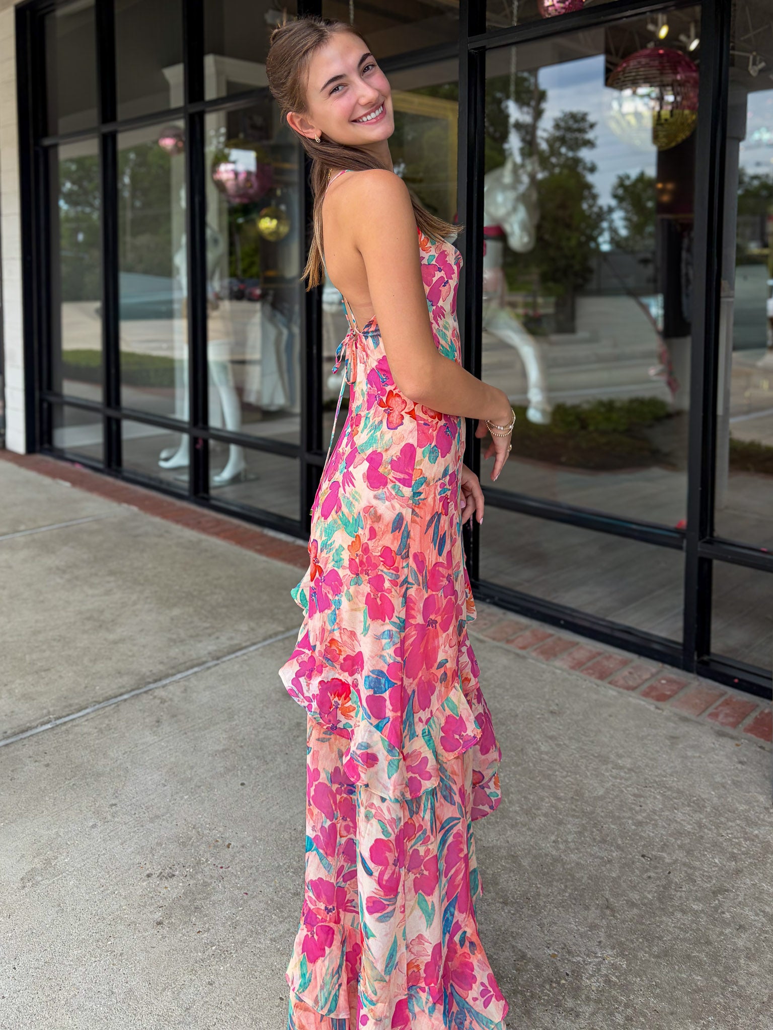 Woman in a floral dress standing outside a building with glass doors.