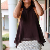 A woman laughing at Rodéo Boutique, wearing a dark brown sheer halter top and a white sequined mini skirt.
