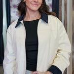 Woman wearing a cream barn jacket with navy cuffs and collar in an indoor setting.