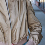 Close-up of a person wearing a beige bomber jacket with a blurred background