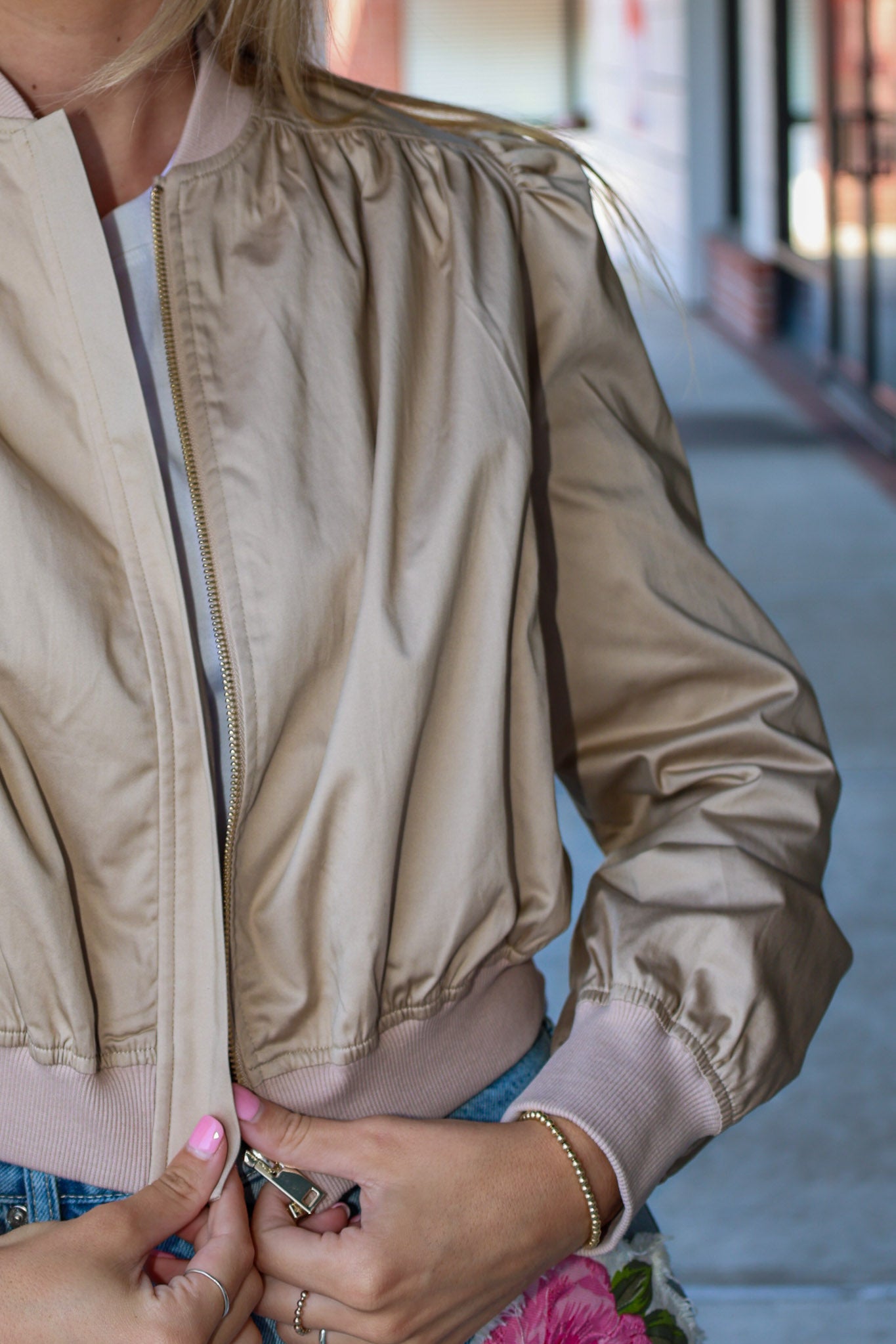 Close-up of a person wearing a beige bomber jacket with a blurred background