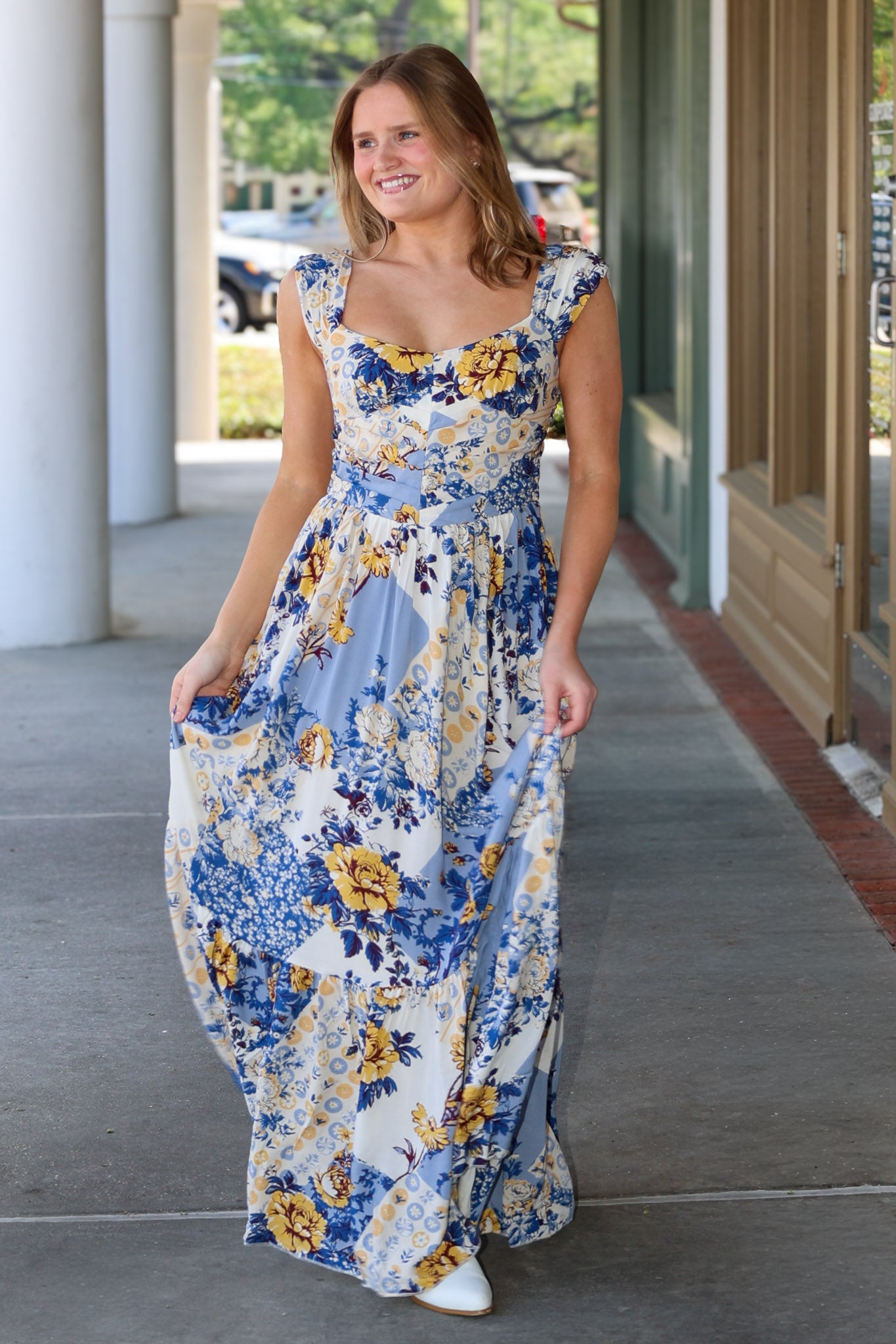 Woman wearing a floral dress standing on a sidewalk.