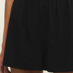 Black shorts worn by a person on a beige background