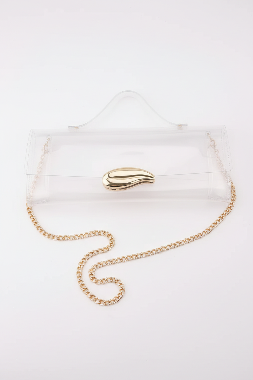 Clear acrylic clutch bag with a gold leaf-shaped clasp and a gold chain strap, shown on a white surface with a black background.