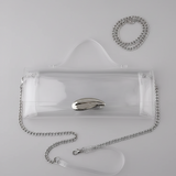 A clear vinyl handbag with a silver chain strap and a metallic silver clasp, displayed on a white surface against a black background.