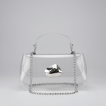 A clear acrylic handbag with a silver chain handle and a faceted silver metal accent on the front, photographed against a neutral light gray background.