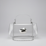 A clear acrylic handbag with a silver chain handle and a faceted silver metal accent on the front, photographed against a neutral light gray background.