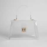 A clear vinyl handbag with a semi-translucent handle, gold-tone hardware, and a small gold clasp on the front, set against a dark gray background.