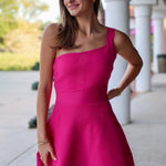 Woman wearing a pink one shoulder mini dress standing outdoors on a sunny day.