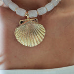 Close-up of a gold shell pendant on a white beaded necklace.
