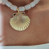 Close-up of a gold shell pendant on a white beaded necklace.